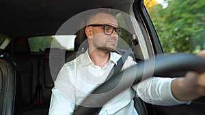 Bearded man in glasses and white shirt driving a car in sunny weather