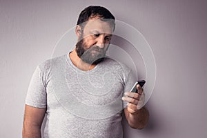 Bearded man in gray t-shirt holding mobile phone, using smartphone, making a call