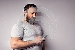 Bearded man in gray t-shirt holding mobile phone, using smartphone, making a call