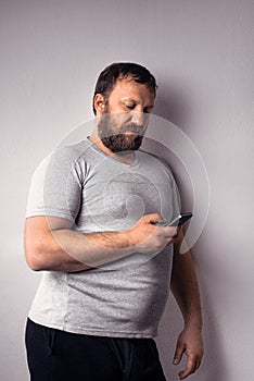 Bearded man in gray t-shirt holding mobile phone, using smartphone, making a call