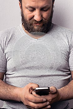 Bearded man in gray t-shirt holding mobile phone, using smartphone, making a call, talking on the phone, texting