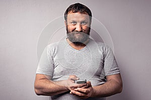 Bearded man in gray t-shirt holding mobile phone, using smartphone, making a call, talking on the phone, texting