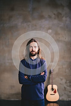 Bearded man with a guitar and posing while standing against wall