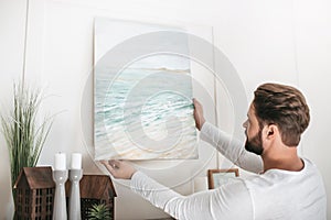 Bearded man hanging picture on wall at home