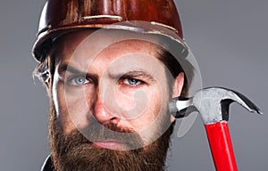 Bearded man in hard hat with hammer. Repair tools. Construction worker, Carpenter in helmet. Closeup.