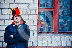 Bearded man in the hat of a buffoon stands near the brick wall