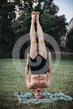 Bearded man headstand balance up in the park. Concept of a healthy lifestyle