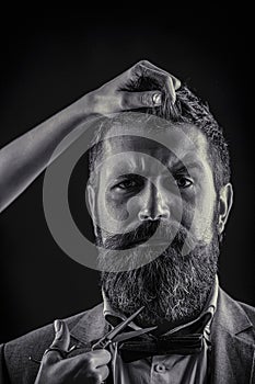 Bearded man hipster barber with beard and moustache in suit holds sharp scissors and cut hair in hairdresser salon