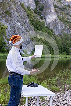 bearded man, hipster in a white shirt and santa hat holds a blank sheet of paper in hand. Reads a speech