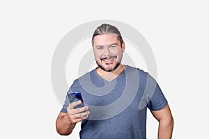 A bearded man in his 30s looks at the camera while browsing on his cellphone. A male of mixed ancestry. Isolated on white