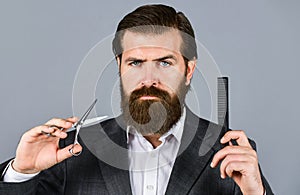 Bearded man hold hair brush and scissors. Confident and handsome brutal man. facial care. Mature hipster with beard