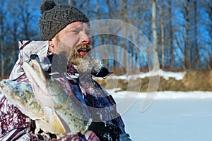 Bearded man is holding frozen fish after successful winter fishing at cold sunny day