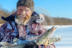 Bearded man is holding frozen fish after successful winter fishing at cold sunny day