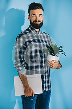 bearded man holding laptop and green plant