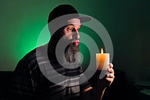 Bearded man holding a lit candle in his hand. Green background