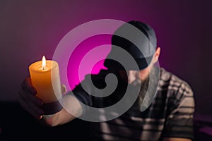 Bearded man holding a lit candle in his hand. Pink background