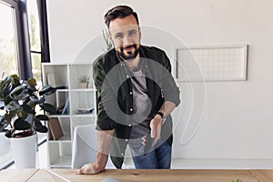 Bearded man holding smartphone and smiling at camera in office
