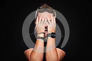 A bearded man holds his hands behind his face and screams in studio on a black background