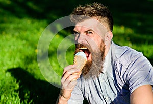 Bearded man with ice cream cone. Temptation concept. Man with long beard eats ice cream, while sits on grass. Man with