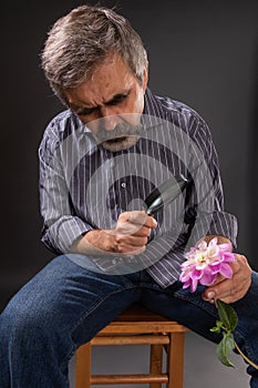 Bearded man with insane stubbornness looks through the magnifying glass the dahlia