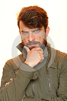 Bearded man in khaki jacket holding his chin. Close.up. White