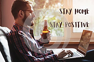 Bearded man with laptop drinking bottle of beer