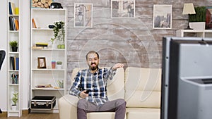 Bearded man laughing while watching tv and holding remote control