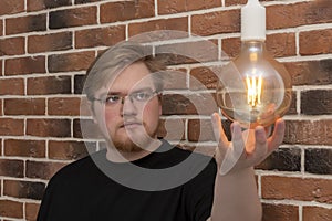 A bearded man with a light bulb on against a brick wall. Concept: connection and disconnection of electricity, room lighting