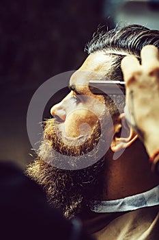 Bearded man with long beard getting hair shaving with razor