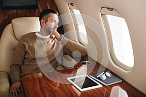 Bearded man looking at airplane window in first class of private jet