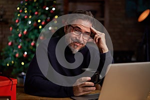 Bearded man looking at camera, using laptop computer at home. Portrait of middle age, mid adult man in 50s shopping online for