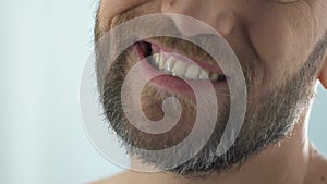 Bearded man looking at teeth in mirror, suffering gum infection pulpitis disease