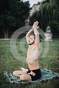 Bearded man in lotus pose sitting on green grass.