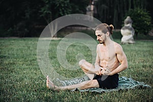 Bearded man in lotus pose sitting on green grass.