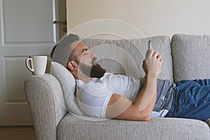 Bearded man lying on sofa with smartphone