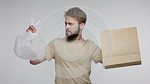 Bearded man making choice between plastic bag and paper package, choosing recyclable eco container, showing like