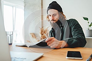 Bearded man making notes while listening virtual lesson