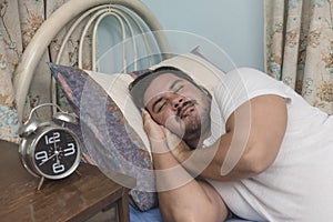 A bearded man of mixed race sleeping soundly on his side on the bed at his apartment. REM sleep