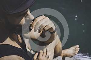 Bearded man model wearing black cap and tshirt looks away, sunset in the sea scenery. Close up portrait.