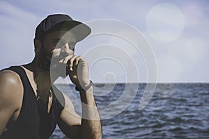Bearded man model wearing black cap and tshirt looks away, sunset in the sea scenery. Visual effects.