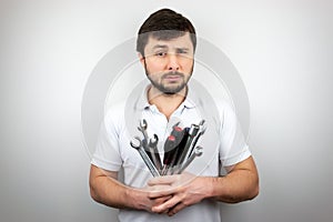 A bearded man with narrowed one eye with a bouquet of wrenches and screwdrivers