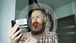 Bearded man online shopping and banking with credit card using smartphone at home