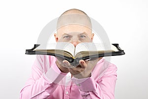 Bearded man in a pink shirt looks through an open Bible