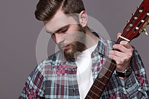 A bearded man in a plaid shirt tunes, plays the guitar