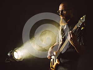 Bearded man playing bass guitar with spotlight