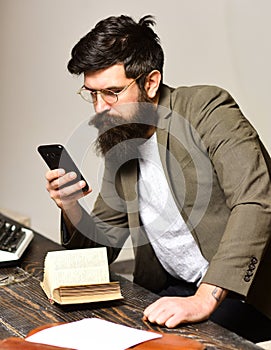 Bearded man in reading glasses with smartphone. Scientist hipster with mobile phone and book. Businessman in suit read