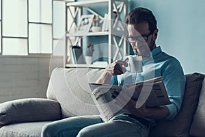 Bearded Man Reading Newspaper on Gray Sofa at Home