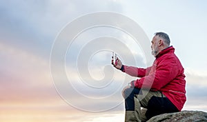 Bearded Man in red jacket relaxing alone on the top of mountain at sunrise.