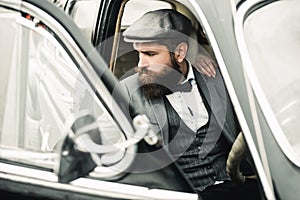 Bearded man in retro car. Brutal guy with mustache in suit near vintage car.