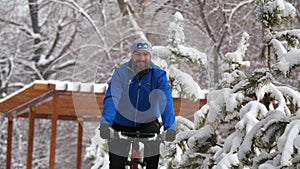 A bearded man rides a bicycle with pleasure in a winter park